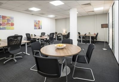 Spacious open-plan coworking area with wooden desks, ergonomic chairs, and colorful wall art.