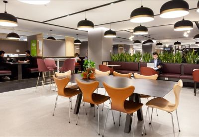 Coworking lounge with warm wood tones, designer chairs, and pendant lighting.