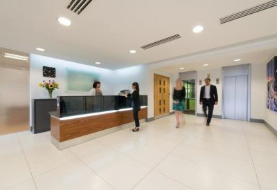 Modern reception area with a wood-fronted desk and people walking through the lobby.