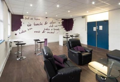 Bright breakout lounge with purple accent walls, recliners, and high-top tables.