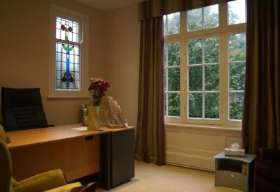 Private office suite with a wooden desk, stained glass window, and professional seating.