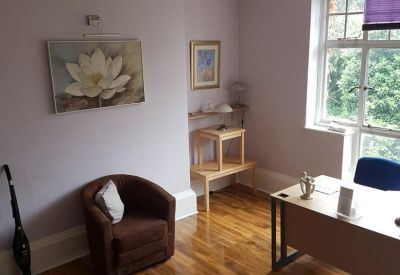 Bright workspace featuring polished wood floors, a purple window blind, and a comfortable brown armchair.