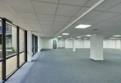 Spacious, empty open-plan office floor with grey carpeting and large windows.