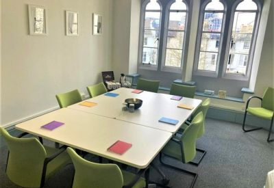 Spacious meeting room at Brighton Forum with a large square table, green chairs, and gothic-style windows.