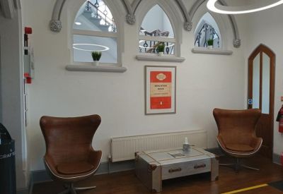 Communal lounge area with brown leather egg chairs, a low coffee table, and arched windows.