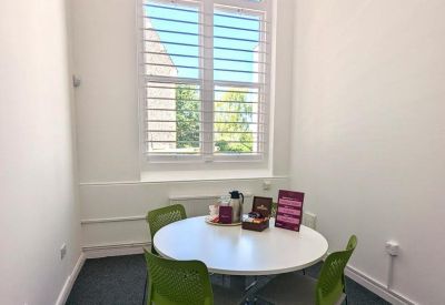 Brightly lit four-person meeting room with a round white table and lime green chairs.
