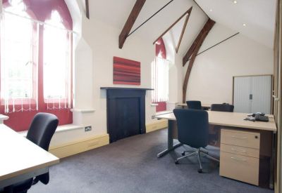 Bright office space featuring wooden ceiling beams, desks, and windows with red privacy screens.
