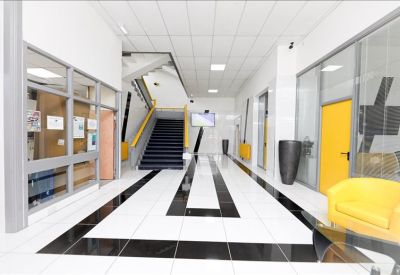 Spacious building lobby with polished black and white tiled floors and a bright yellow armchair.