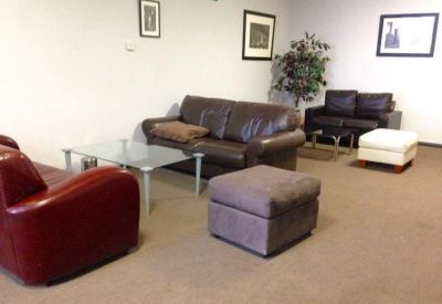 Communal lounge area featuring brown leather sofas, a red armchair, and a glass coffee table.