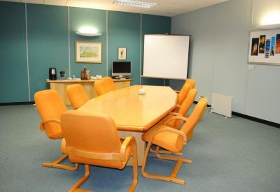 Bright boardroom with an oval light wood table and vibrant orange chairs.