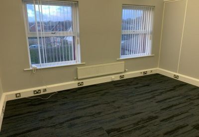 Spacious empty office room with dark grey carpet and two large windows.