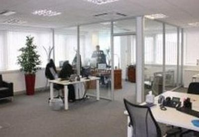 Glass-partitioned private office suites with white desks and ergonomic chairs.