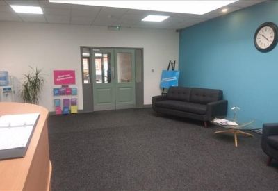 Spacious reception area with a blue feature wall, black sofas, and a wall clock.
