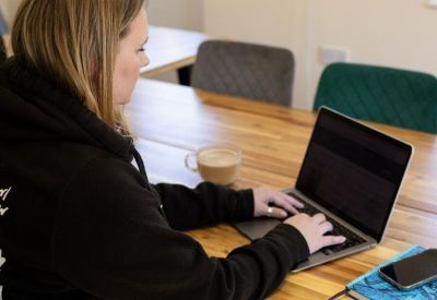 A person working on a laptop at a long wooden communal desk with a coffee mug.