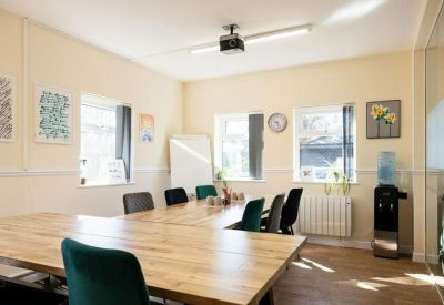 Spacious meeting room with wooden tables, green chairs, and a ceiling projector.