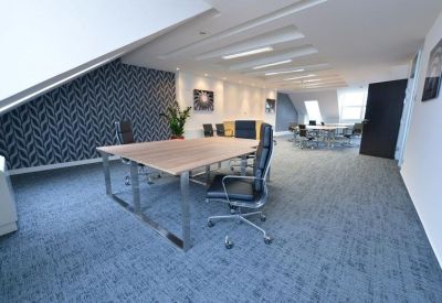 Spacious open-plan office under a sloped ceiling with modern desks and patterned feature wall.