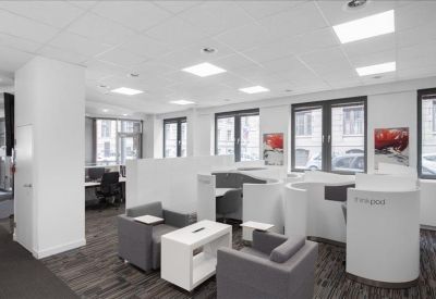 Breakout area with grey armchairs, white coffee table, and semi-private workstations.