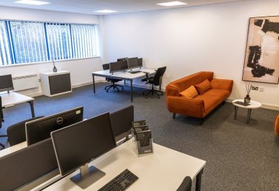 Furnished office space featuring a bright orange sofa and white workstations.
