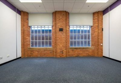 Empty office space with blue carpet and large industrial windows framed by exposed red brick.