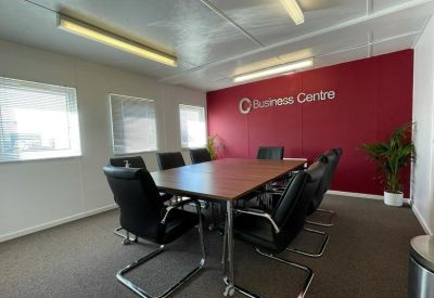 Bright meeting room with a wooden table, black leather chairs, and a red accent wall.
