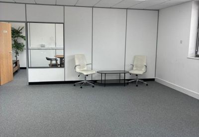Spacious communal breakout area with grey carpeting and white accent chairs.