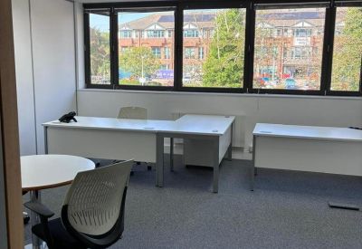 Private office suite with multiple desks and large windows overlooking local buildings.