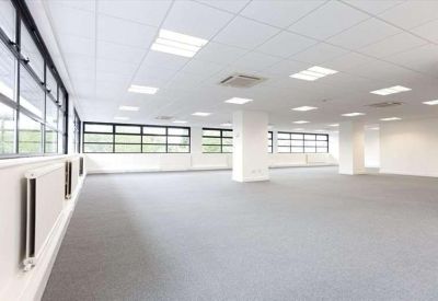 Spacious open-plan office area with white columns and large windows providing natural light.
