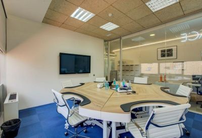 Circular meeting table with ergonomic white chairs and a large wall-mounted screen.