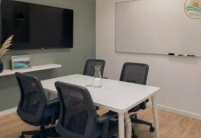 Bright meeting room with a white table, four ergonomic mesh chairs, a large TV, and a whiteboard.