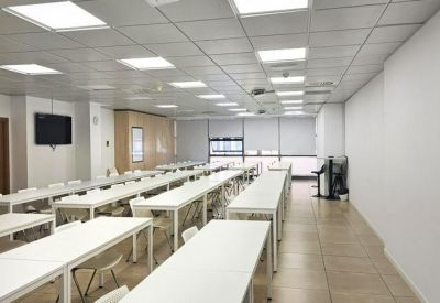 Large canteen or assembly room with many long white tables and bright overhead lighting.