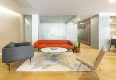 Modern lobby with an orange sofa and designer armchairs on a patterned rug.