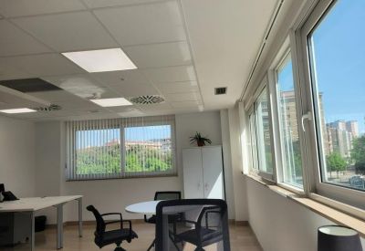 Bright private office featuring a round meeting table, workstations, and large windows with blinds.