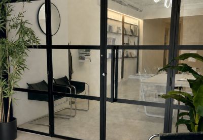 Reception area seen through a black-framed glass door with a large round mirror.