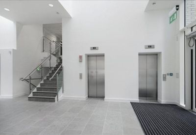 Modern building lobby with polished tile flooring, two elevators, and a metal-railed staircase.