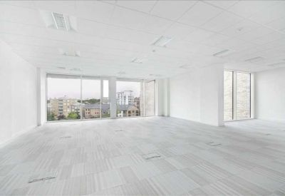 Spacious open-plan office with white walls and floor-to-ceiling windows showing city views.