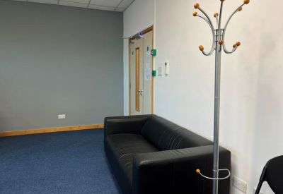 Waiting area with a black leather sofa, blue carpet, and a modern silver coat rack.