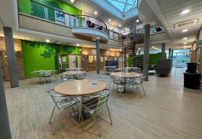 Spacious communal atrium with circular tables, a spiral staircase, and a green feature wall.