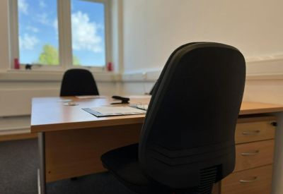 Private office suite featuring a wooden desk, black office chair, and a large window.