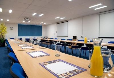 Spacious meeting room with a long boardroom table and dual presentation screens.