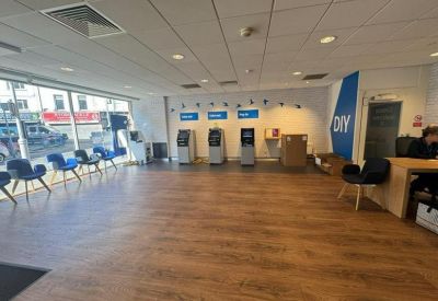 Spacious reception area with wood-effect flooring, blue seating, and automated service machines.