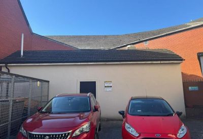 Rear view of the building with a small parking area and two red cars.