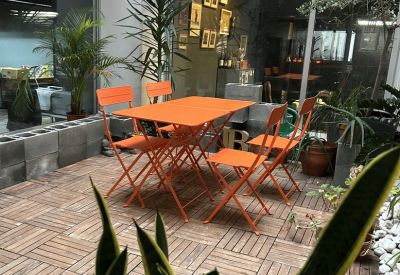 Sunlit communal patio area with bright orange folding tables and chairs surrounded by plants.