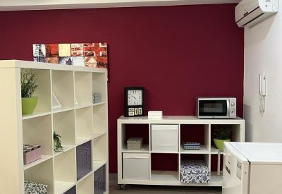 Communal break area with a white shelving unit, microwave, and small fridge against a burgundy wall.