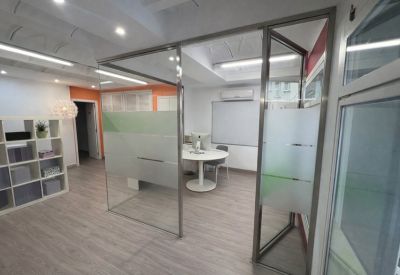 Modern office entrance area with glass partitions and a glimpse into a private meeting room.