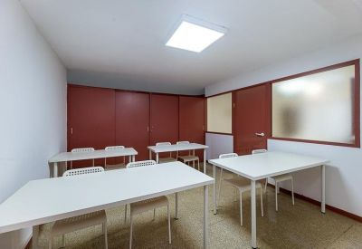 Versatile common room with several white tables, red doors, and a glass partition.