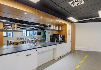 Sleek kitchenette with white cabinetry, black countertops, and a coffee machine.