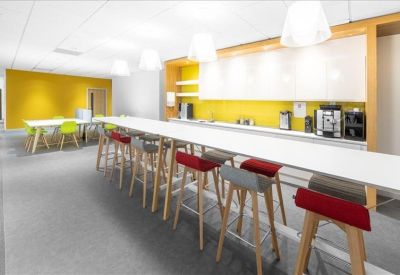 Communal kitchen and break area with long breakfast bar, red stools, and bright yellow backsplash.