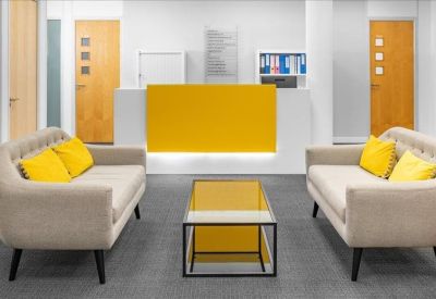 Bright reception area with a yellow front desk and two neutral sofas with yellow cushions.