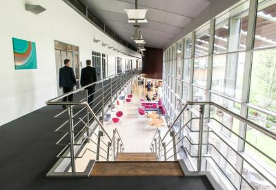 Modern hallway with glass windows looking down onto a vibrant communal lounge area.