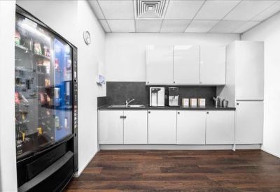 Staff kitchen and breakout area with white cabinetry, wood-effect flooring, and a vending machine.